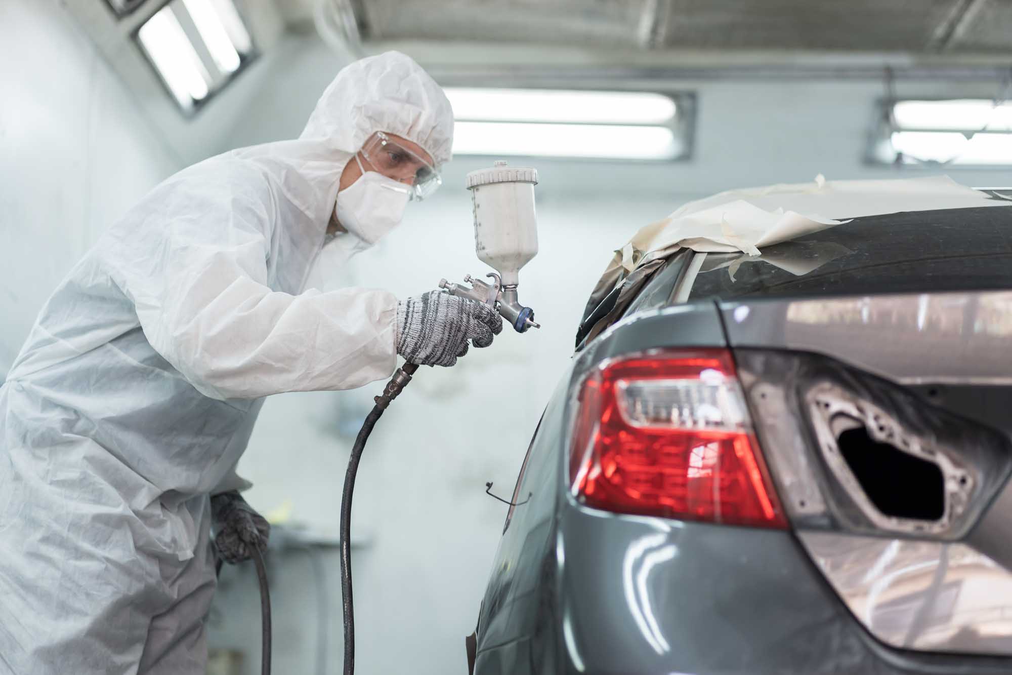 Painter in booth spraying silver car - Advanced Auto Solutions collision repair services 